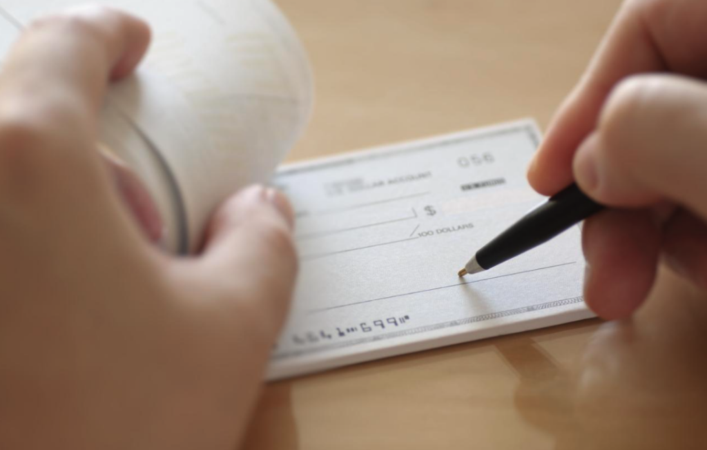 Person writing a check with a pen on a checkbook